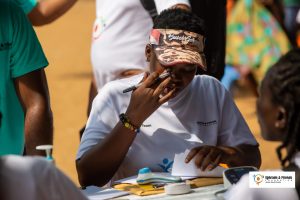 A volunteer from Ephraim & Friends Foundation carefully takes notes during a community health outreach event, ensuring accurate documentation